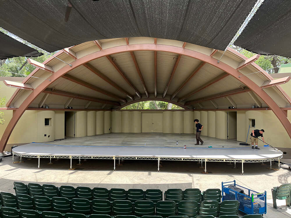 Outdoor stage setup with steel deck platform for film grip and rigging, featuring workers preparing the stage area.