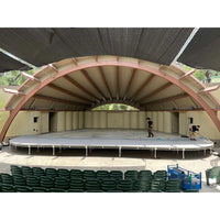 Outdoor stage setup with steel deck platform for film grip and rigging, featuring workers preparing the stage area.